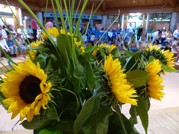 ein Strauß Sonnenblumen, im Hintergrund eine voll besetzte Aula © Nora Leiner